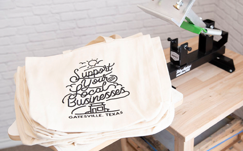 a stack of tote bags that say support your local businesses sitting on a platen