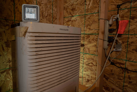 a dehumidifier and hygrometer sit in a plywood drybox