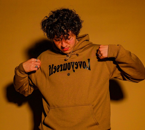 A man wears a tan hoodie with the words "love yourself" spelled backwards