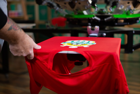 Una mano saca una camisa de poliéster estampada roja de una platina