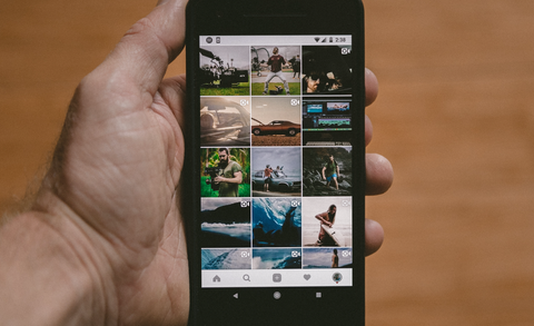 A hand holds a phone displaying an Instagram feed