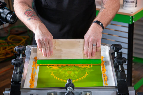 A printer pulls a squeegee over a screen