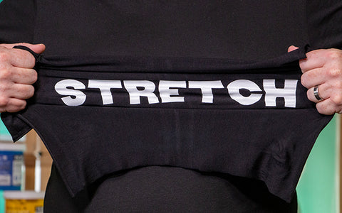 a man stretches a black shirt printed with white ink that reads "Stretch"