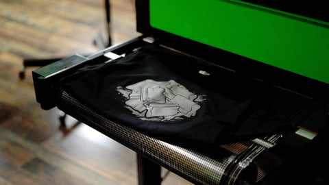 A black shirt printed with Stretch ink comes out of the conveyor dryer