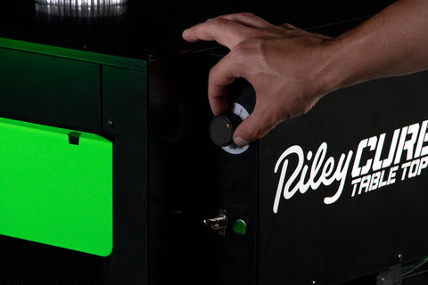 A hand adjusts the Riley Cure tabletop knob