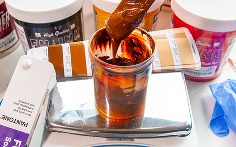 a mixing container with brown ink and a pantone matched book behind it