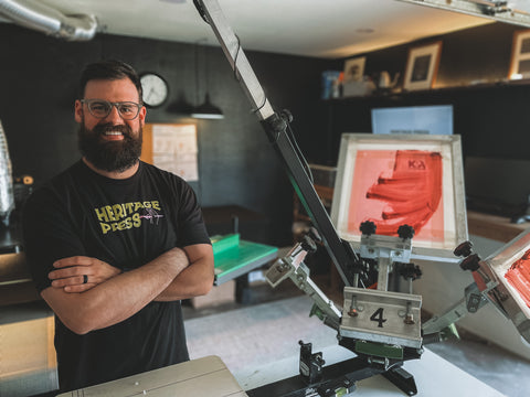 A man folds his arms and stands in front of a printing press with a laser attachment