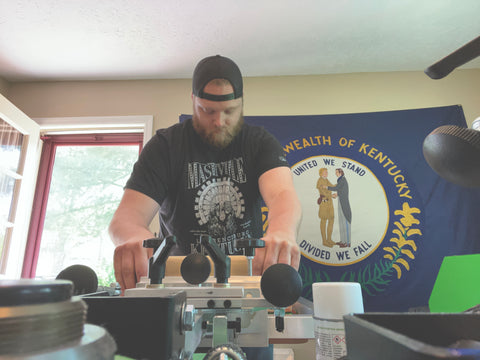 A man prints in a shop with the Kentucky flag behind him