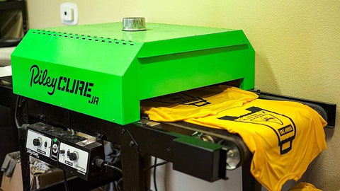 A yellow shirt with a black design on it comes out of a Riley Cure conveyor dryer