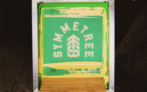 a screen on press that says symmetree with gold ink and a squeegee