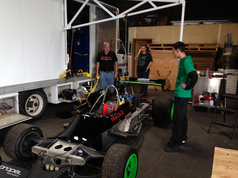 Riley Hopkins standing with his race car and two employees