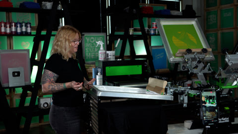 a woman stands in front of a press with the screen down on a platen