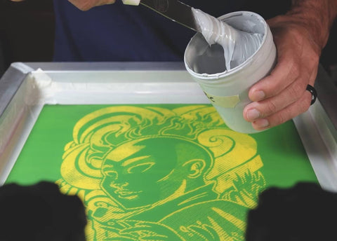 A man spreading white ink with a spatula onto a screen