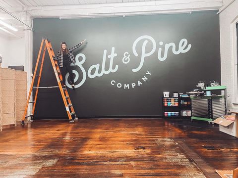 printer standing on a ladder in front of their mural. mural says salt & pine company