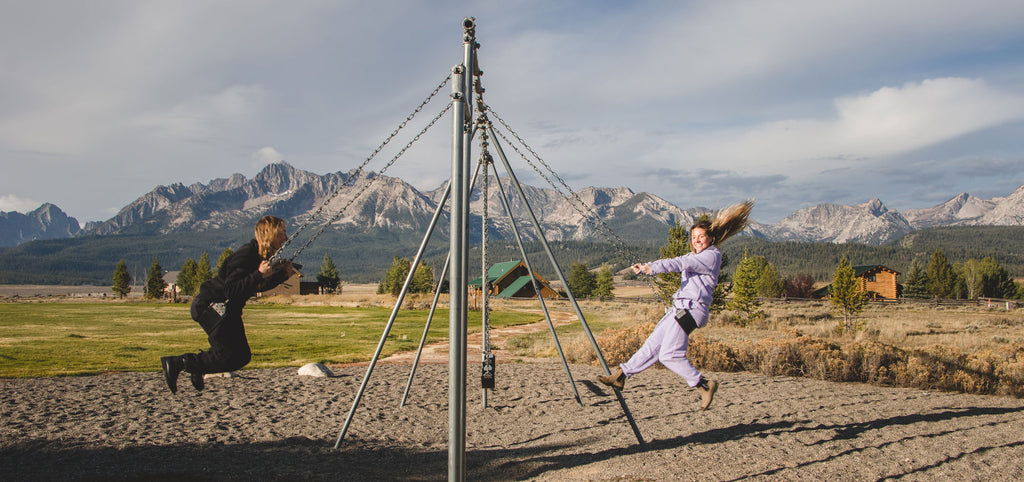 image shows two girls in matching fleece sets on a swing set in front of mountains