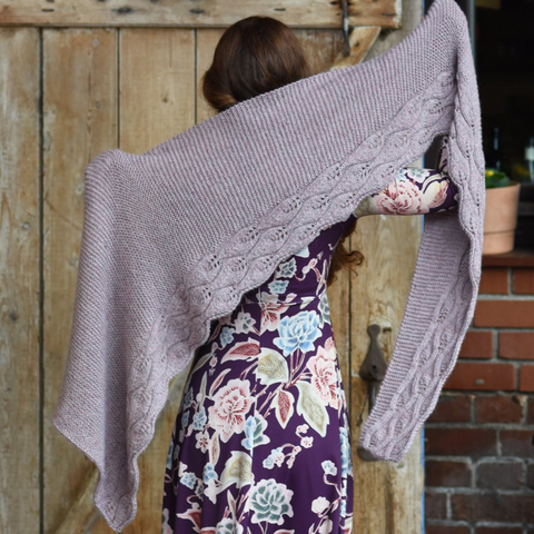 Woman wearing a purple floral dress holding a knit shawl in a lavender yarn. 