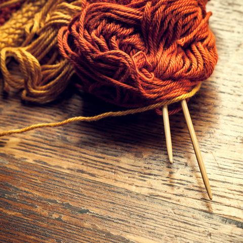 Yarn in warm gold and copper colors with wooden knitting needles on a wooden table.