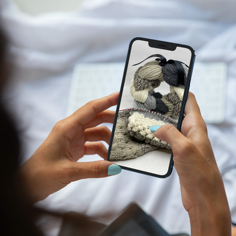 Woman holding a cell phone with an image of yarn and a knit project on it.