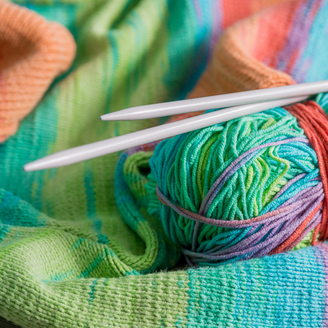 Brightly colored self-striping yarn with knitting needles on knit stockinette fabric.