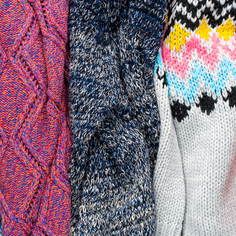 Three knit sweaters in fuschia, marled gray and colorwork featuring white, black, yellow, pink and blue.