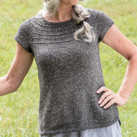 Woman wearing a dark gray short-sleeved sweater standing in a grassy field.