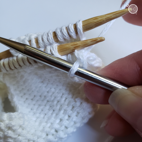 White yarn on wooden needles with one stitch on a third metal needle.