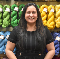 Headshot of Tricia Miranda-Hartsuff standing in front of a wall of displayed yarn.