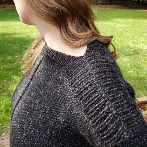Close up of ribbing detail on the shoulder of a black heathered knit sweater.