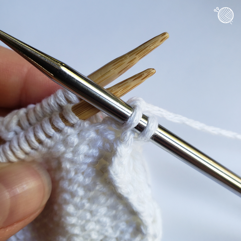 White yarn on wooden needles with two stitches on a third metal needle.
