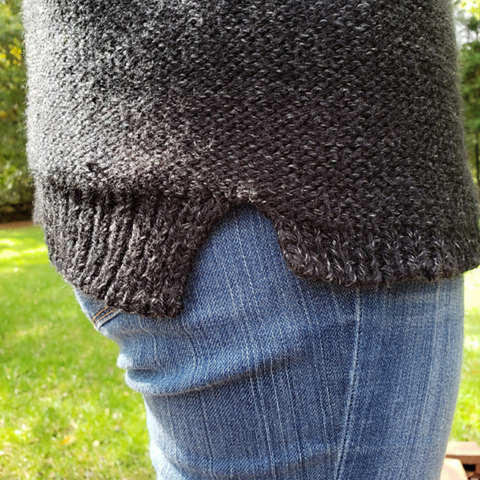 Close up of split hem detail on a heathered black knit sweater.