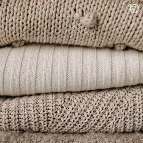 Stack of folded sweaters in natural colors.