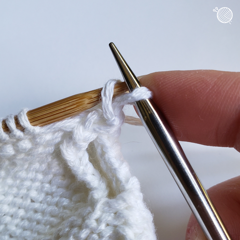 White yarn on wooden needle moving stitch up and over on a metal needle.