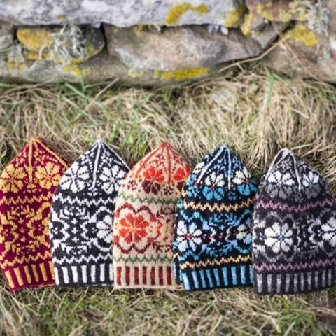 Five fair isle knit beanies lined up along an old stone wall.