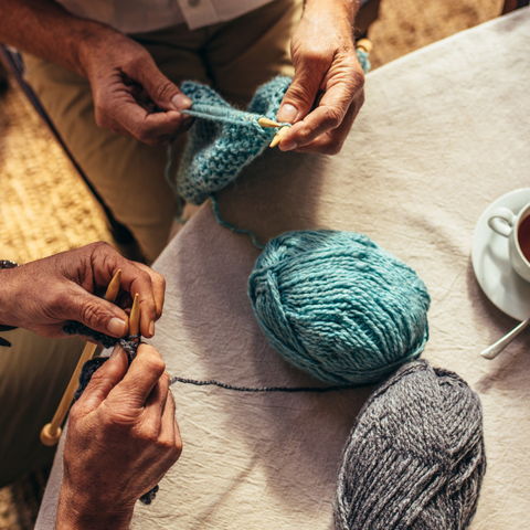 Overhead image of hands knitting with balls of yarn on a table.