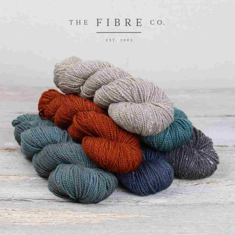 A pile of Acadia yarn in grays, blues and red from The Fibre Company.