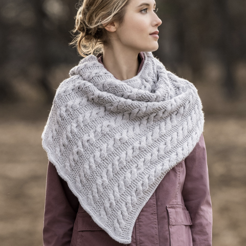 Woman standing in a field wearing a light gray Livonia Shawl looking into the distance.