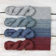 Four skeins of Acadia yarn from The Fibre Co. in gray, blues and deep red.