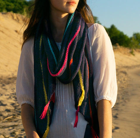 Woman wearing a knit navy blue shawl with colorful stripes on a sandy dune.