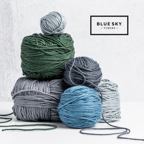 four balls of yarn in green, blue, and grey shades stacked on top of one another.