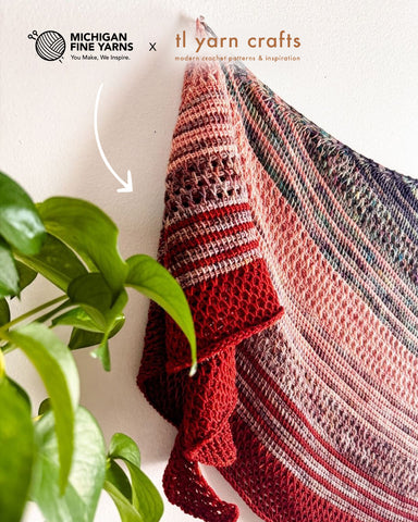 Tunisian crochet scarf displayed on a wall behind bright green foliage.