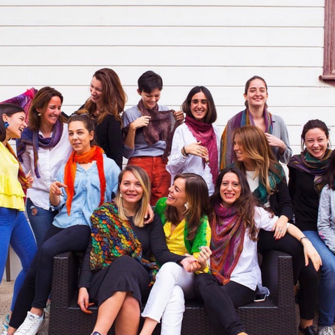 A group of women smiling and laughing - most of whom are wearing knit garments or accessories.