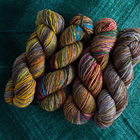 Four skeins of different multicolored yarns on a teal background.