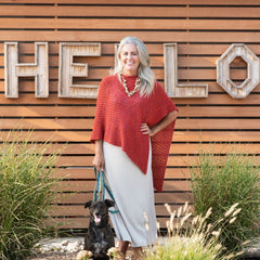 Orangey knit poncho modeled against wood slat wall backdrop with dog.