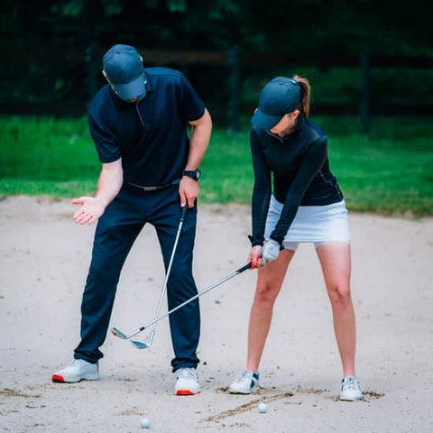 golf instructor teaching golfer how to hit out of bunker