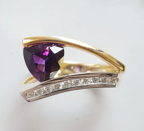 A split shank two tone ring in 14k white and yellow gold, with a channel set row of diamonds in white gold, and a plain yellow gold bar supporting a trillion cut AZ Amethyst.