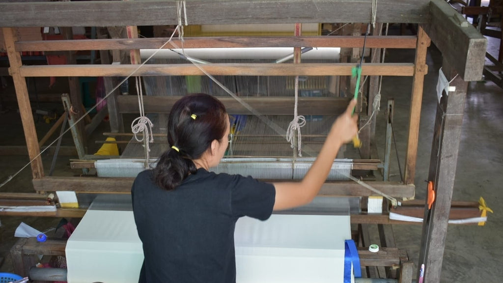 Image shows the back of a handweaver creating 100% silk fabric on a traditional loom.