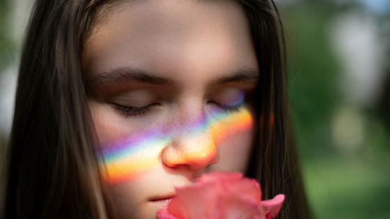 Woman smelling a rose with rainbow reflecting on her face 