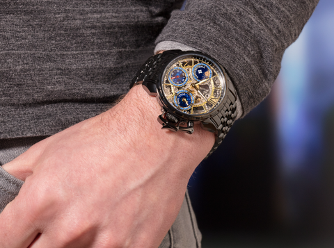 Tufina Oman from the Theorema collection. This is a black skeleton dial watch with three blue sub-dials, sword hands, day and night indicator and a black stainless steel bracelet.