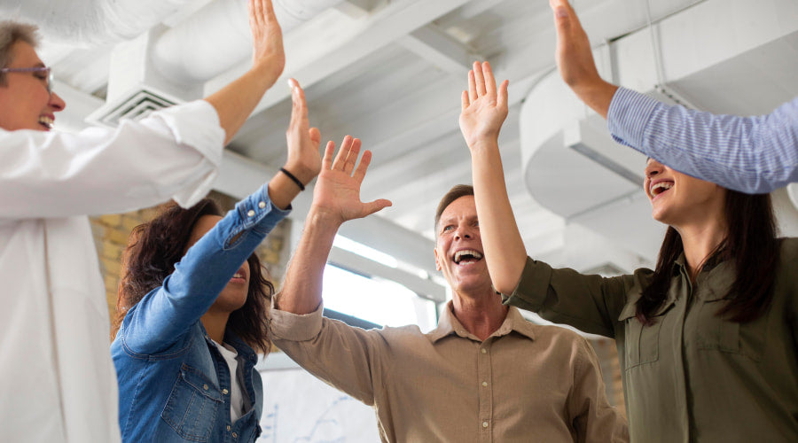 Four co-workers high-fiving happily in an office setting