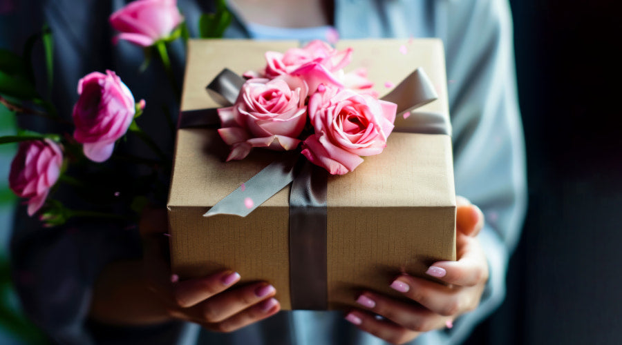 A person holding a gift box adorned with pink roses and a ribbon